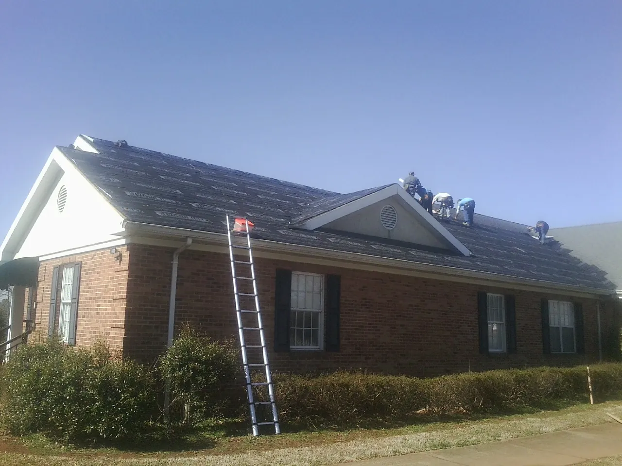 Crew tearing shingles off a brick ranch roof with a ladder set — Metal Roof Repair work by our crew in Speedwell